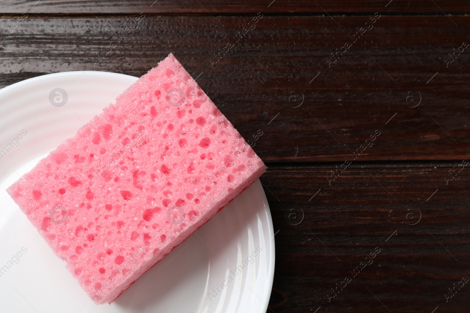 Photo of Pink sponge and plate on wooden table, top view. Space for text