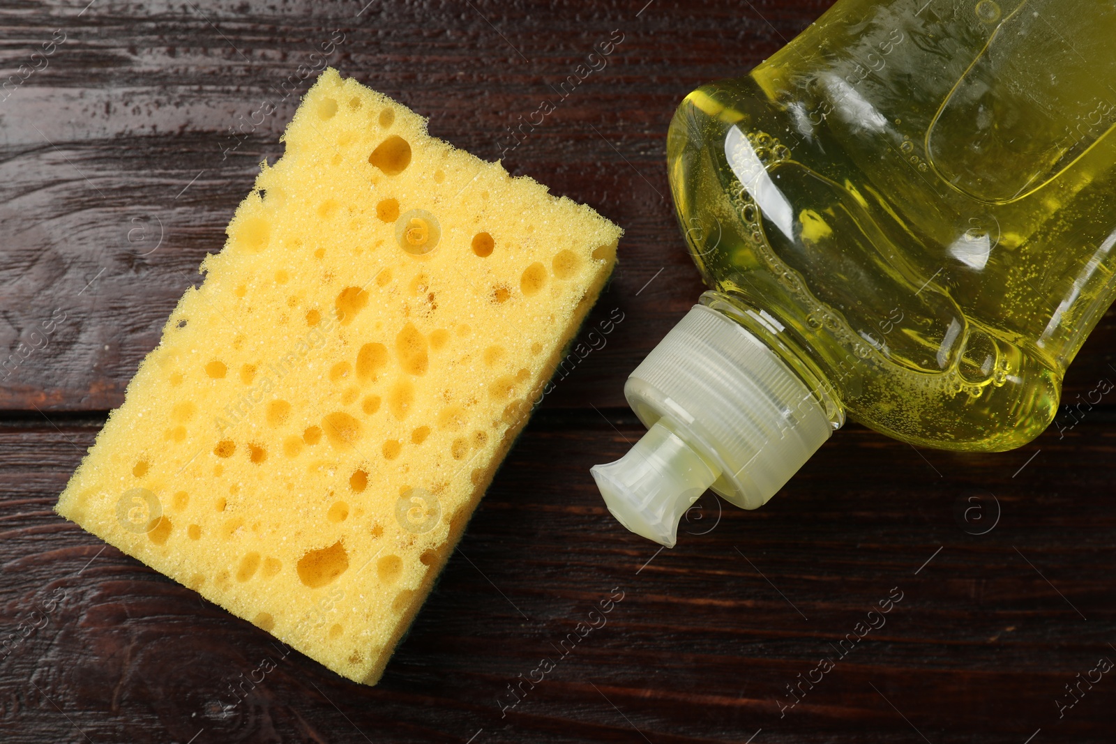 Photo of Yellow sponge and dish soap on wooden table, flat lay