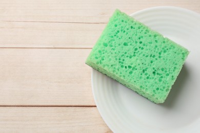 Photo of Green sponge and plate on wooden table, top view. Space for text