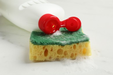 Photo of Soft sponge with foam and dish soap on white table, closeup