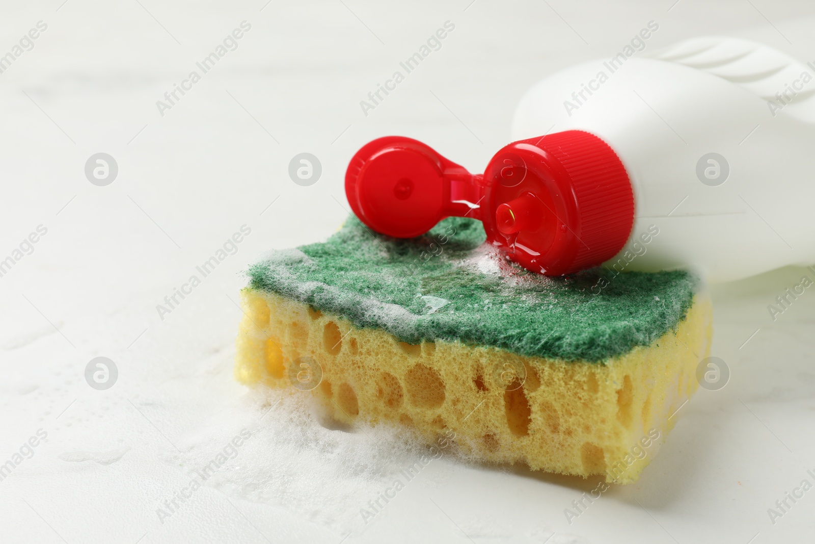 Photo of Soft sponge with foam and dish soap on white table, closeup. Space for text