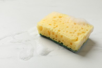 Photo of Yellow sponge with foam on white background, space for text