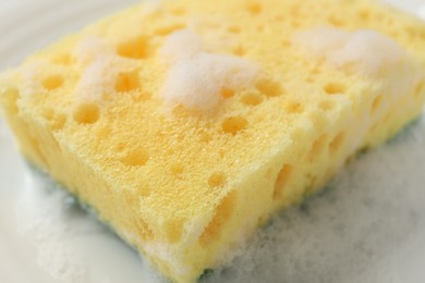 Photo of Yellow sponge with foam on plate, closeup