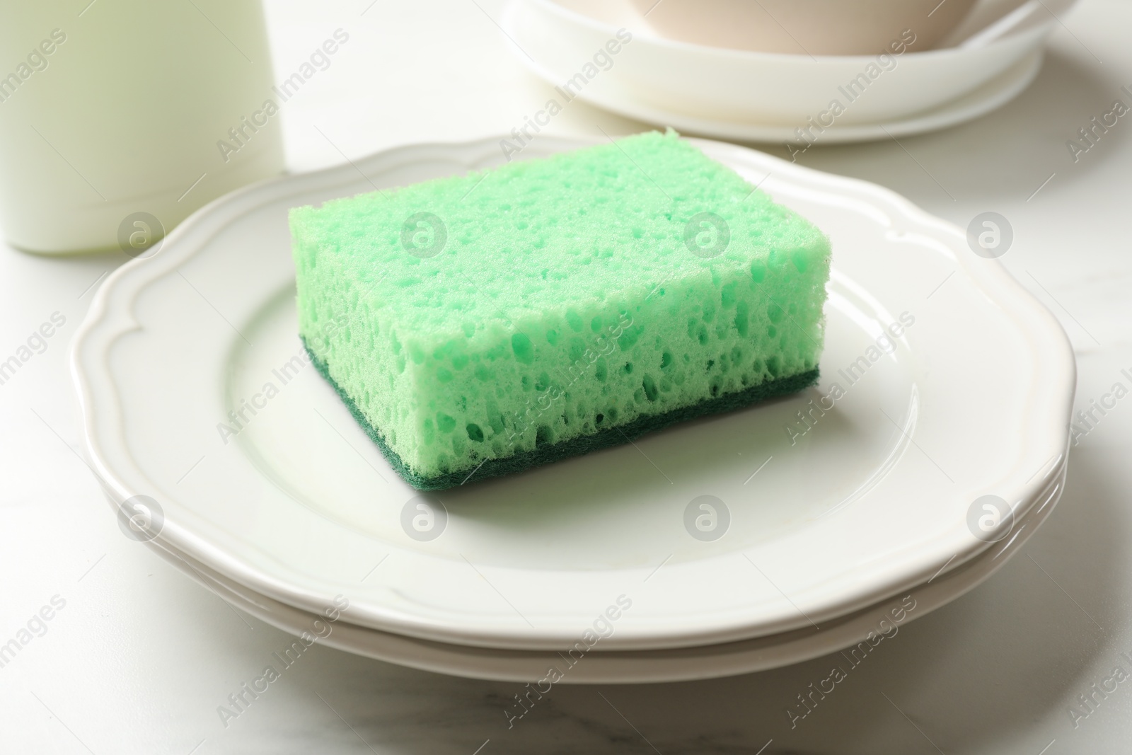 Photo of Green sponge and plates on white table, closeup