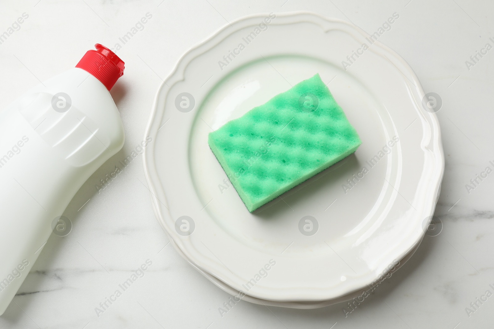 Photo of Green sponge, plate and dish soap on white table, flat lay