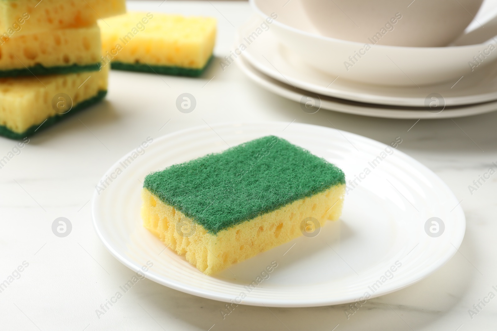 Photo of Yellow sponges and dishware on white table, closeup