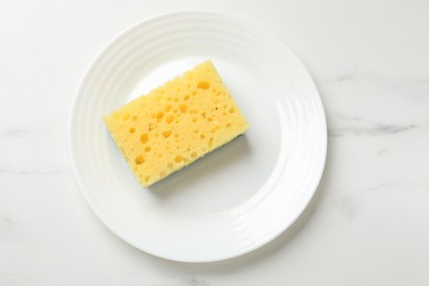 Photo of Yellow sponge and plate on white table, top view