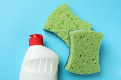 Photo of Green sponges and dish soap on light blue background, flat lay