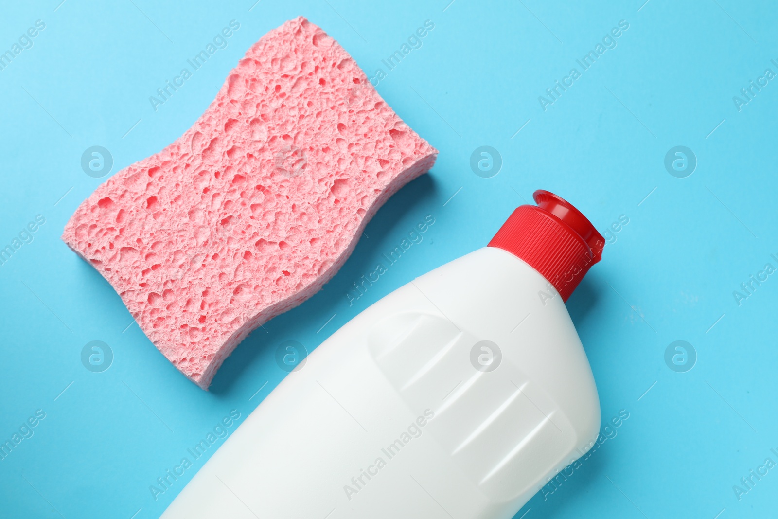 Photo of Pink sponge and dish soap on light blue background, flat lay