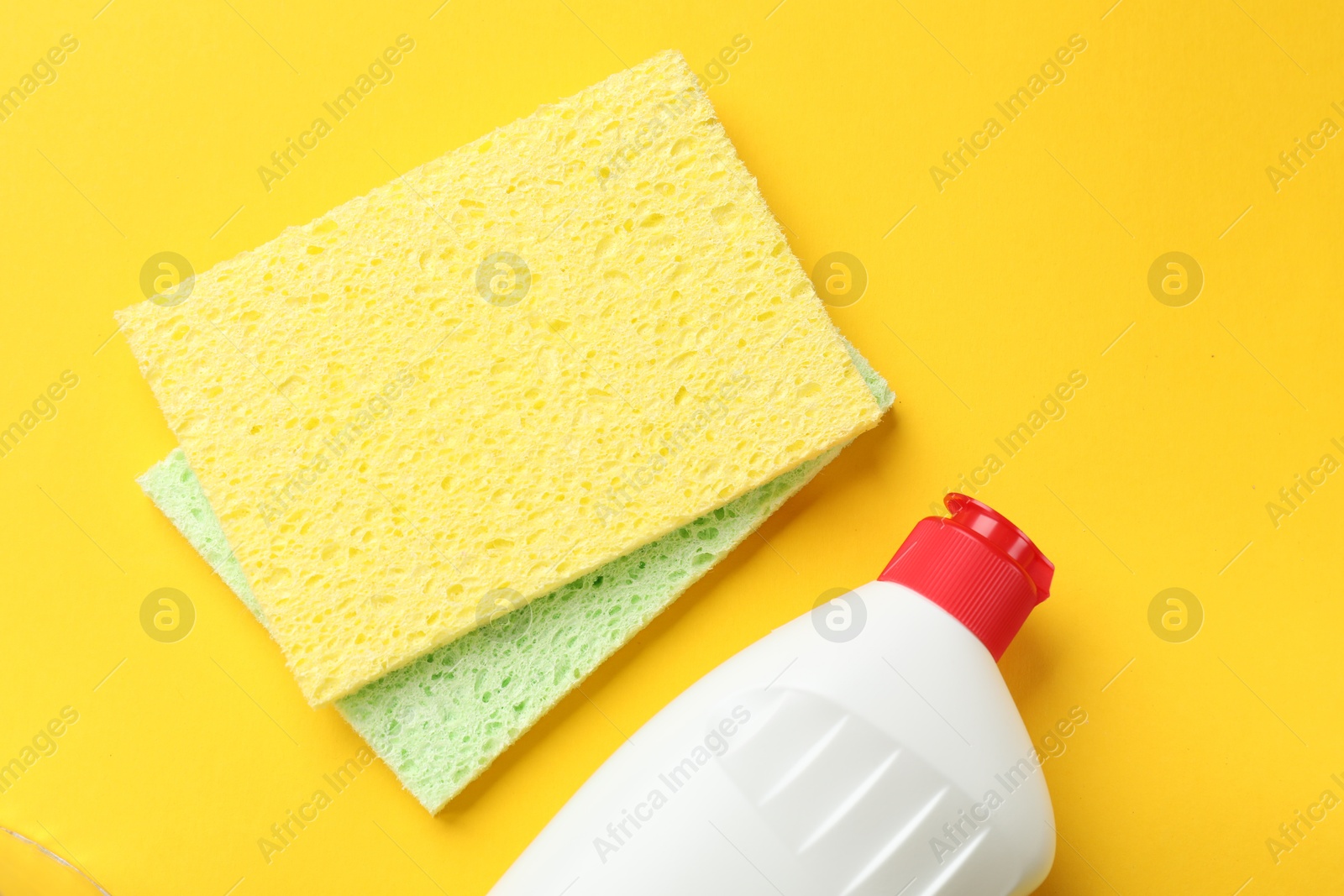 Photo of Soft sponges and dish soap on yellow background, flat lay