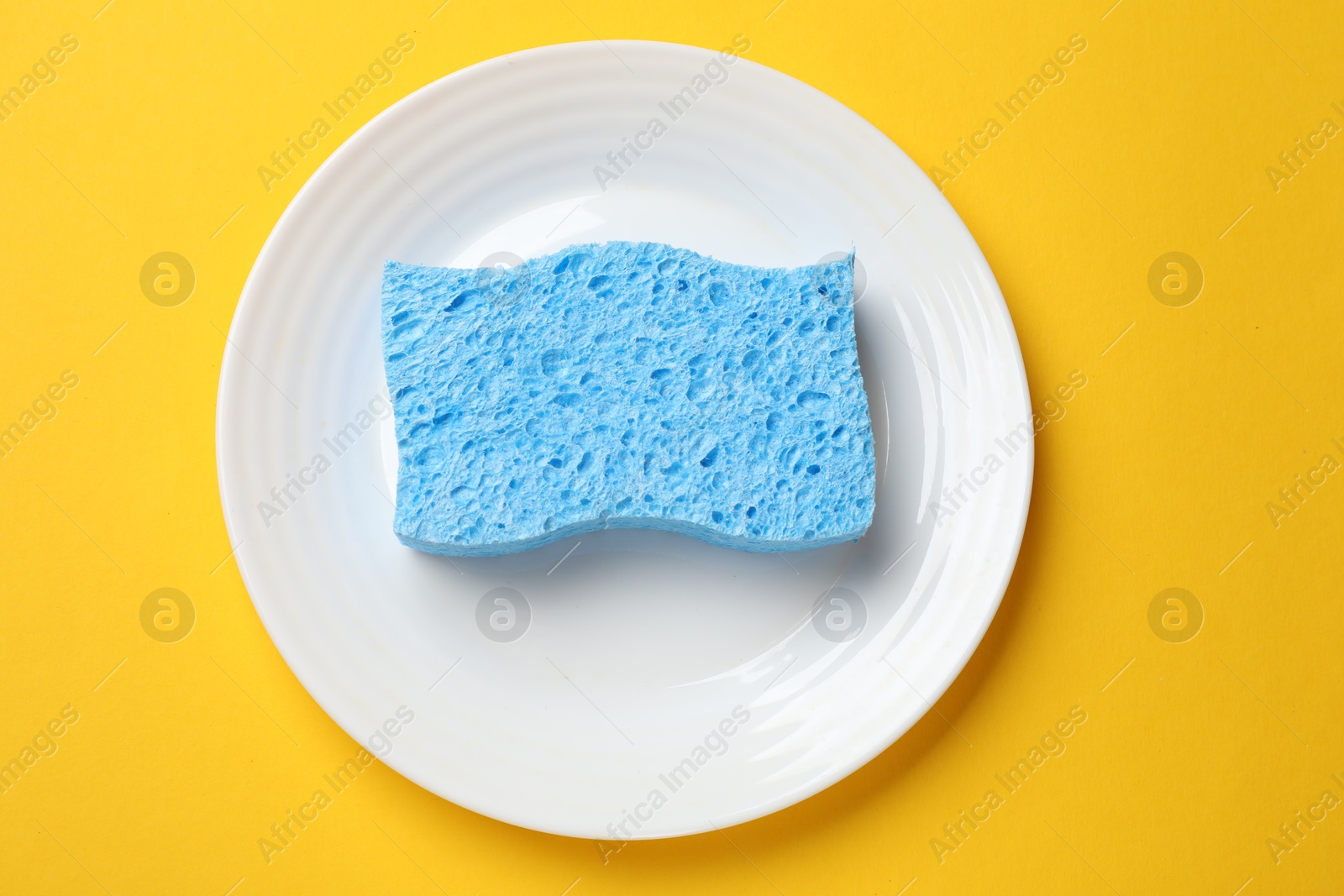 Photo of Light blue sponge and plate on yellow background, top view