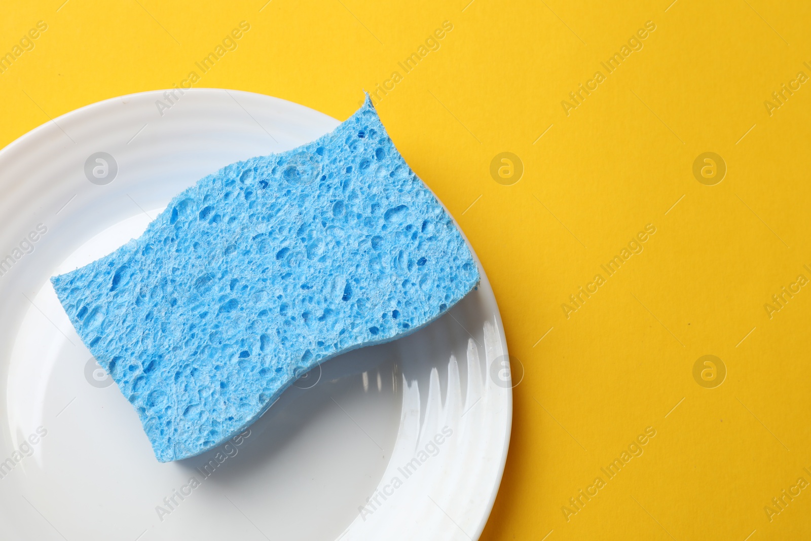 Photo of Light blue sponge and plate on yellow background, top view. Space for text