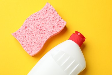 Photo of Pink sponge and dish soap on yellow background, flat lay