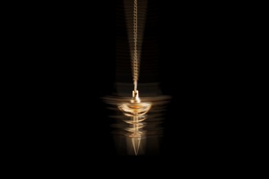 Image of Hypnosis session. Golden pendulum swinging on black background, motion blur effect