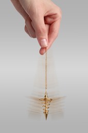 Image of Hypnosis session. Woman swinging golden pendulum on grey background, motion blur effect