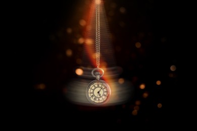 Image of Hypnosis session. Vintage pocket watch swinging on black background, motion blur effect. Magic lights