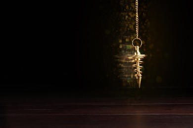 Image of Hypnosis session. Golden pendulum swinging on black background, motion blur effect. Magic lights