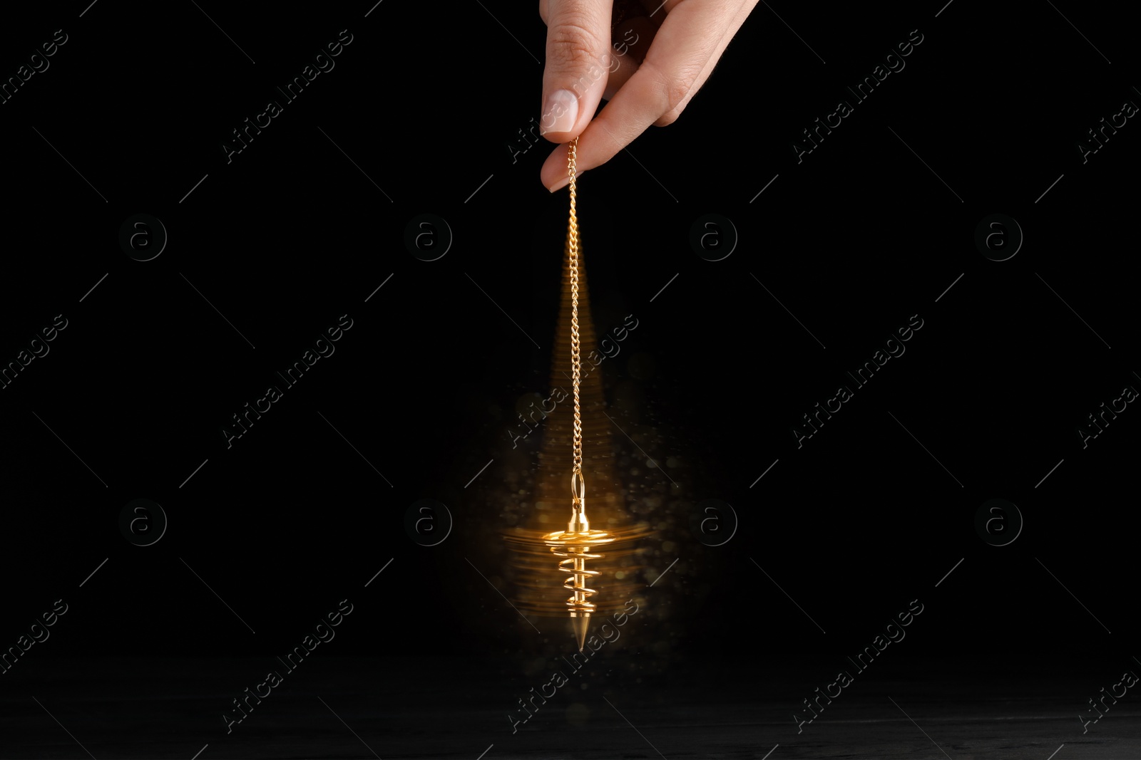 Image of Hypnosis session. Woman swinging golden pendulum on black background, motion blur effect. Magic lights