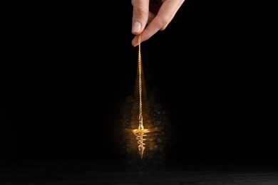 Image of Hypnosis session. Woman swinging golden pendulum on black background, motion blur effect. Magic lights