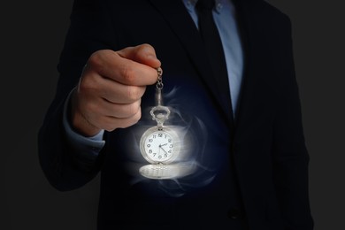 Image of Hypnosis session. Man swinging vintage pocket watch on dark background, motion blur effect. Magic waves