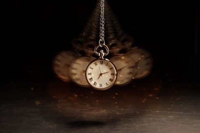 Image of Hypnosis session. Vintage pocket watch swinging on black background, motion blur effect. Magic lights