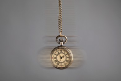 Image of Hypnosis session. Vintage pocket watch swinging on grey background, motion blur effect