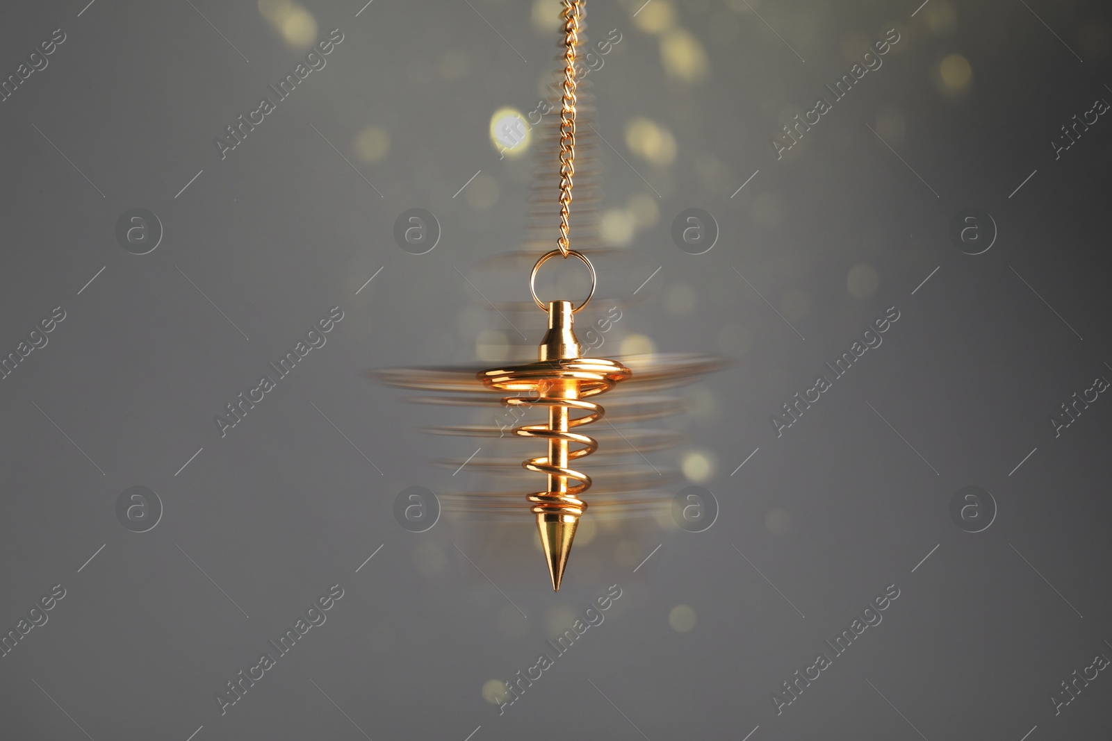 Image of Hypnosis session. Golden pendulum swinging on grey background, motion blur effect. Magic lights