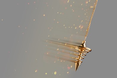 Image of Hypnosis session. Golden pendulum swinging on grey background, motion blur effect. Magic lights