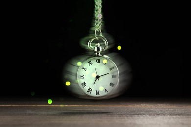 Image of Hypnosis session. Vintage pocket watch swinging on black background, motion blur effect. Magic lights