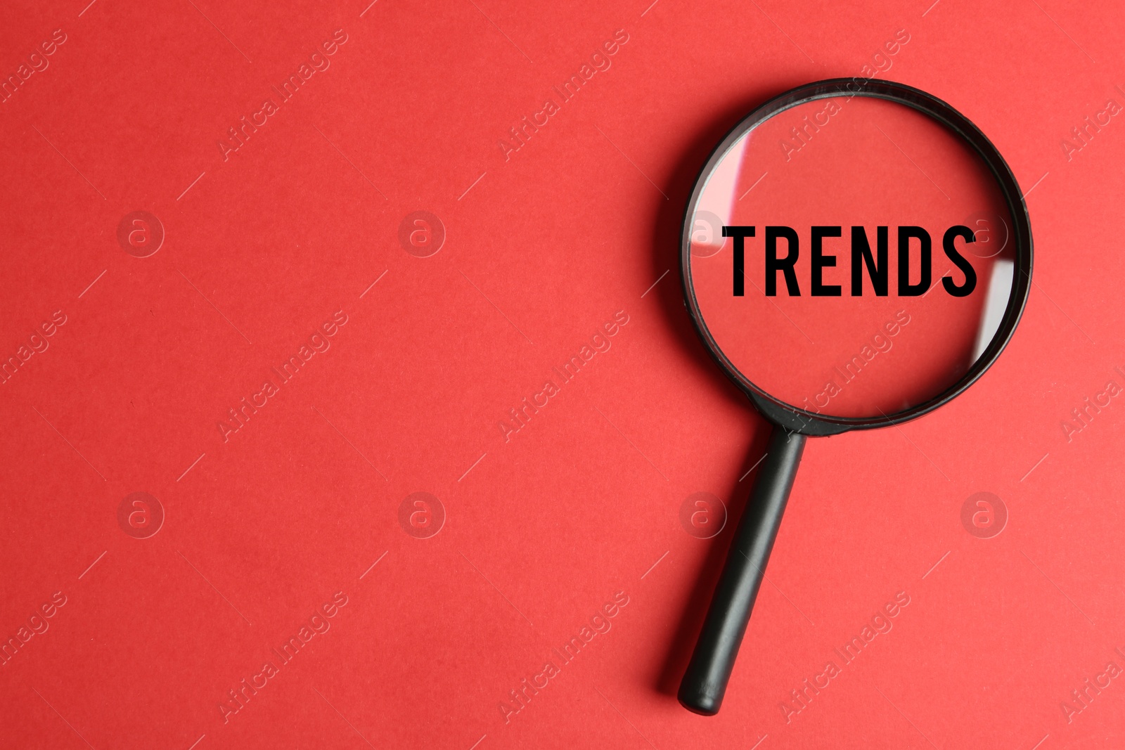 Image of Word Trends on red background, view through magnifying glass. Concept of searching for new and popular ideas