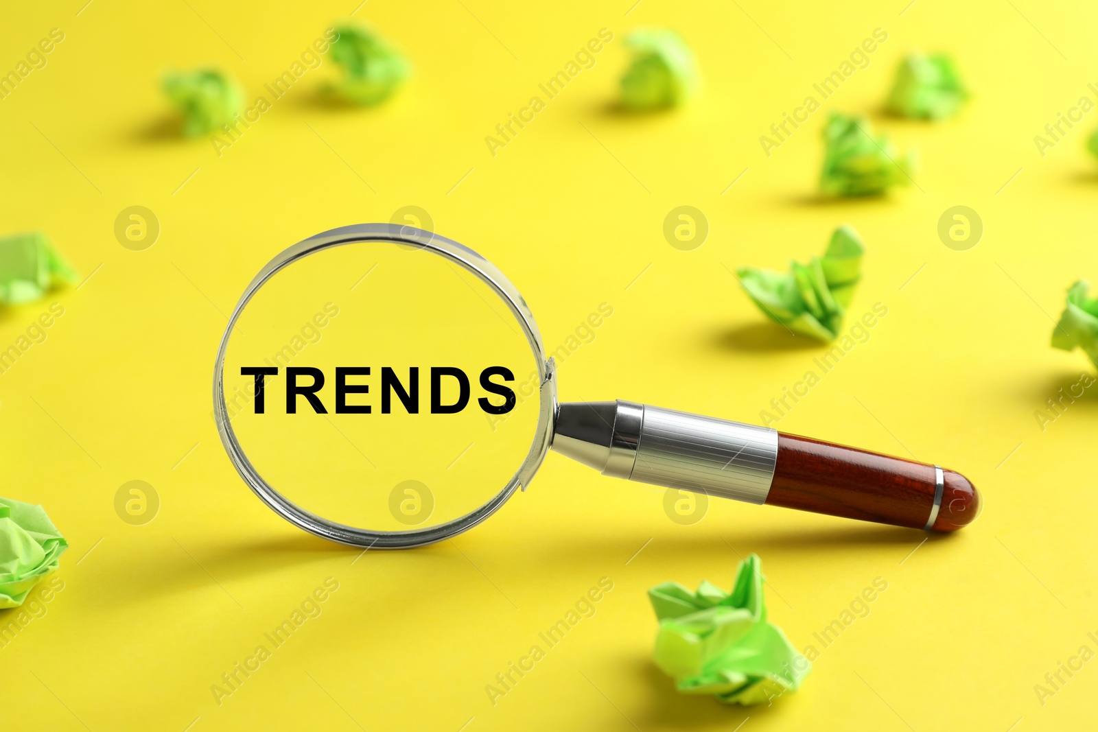 Image of Word Trends in magnifying glass among crumpled paper balls on yellow background, closeup. Concept of searching for new and popular ideas