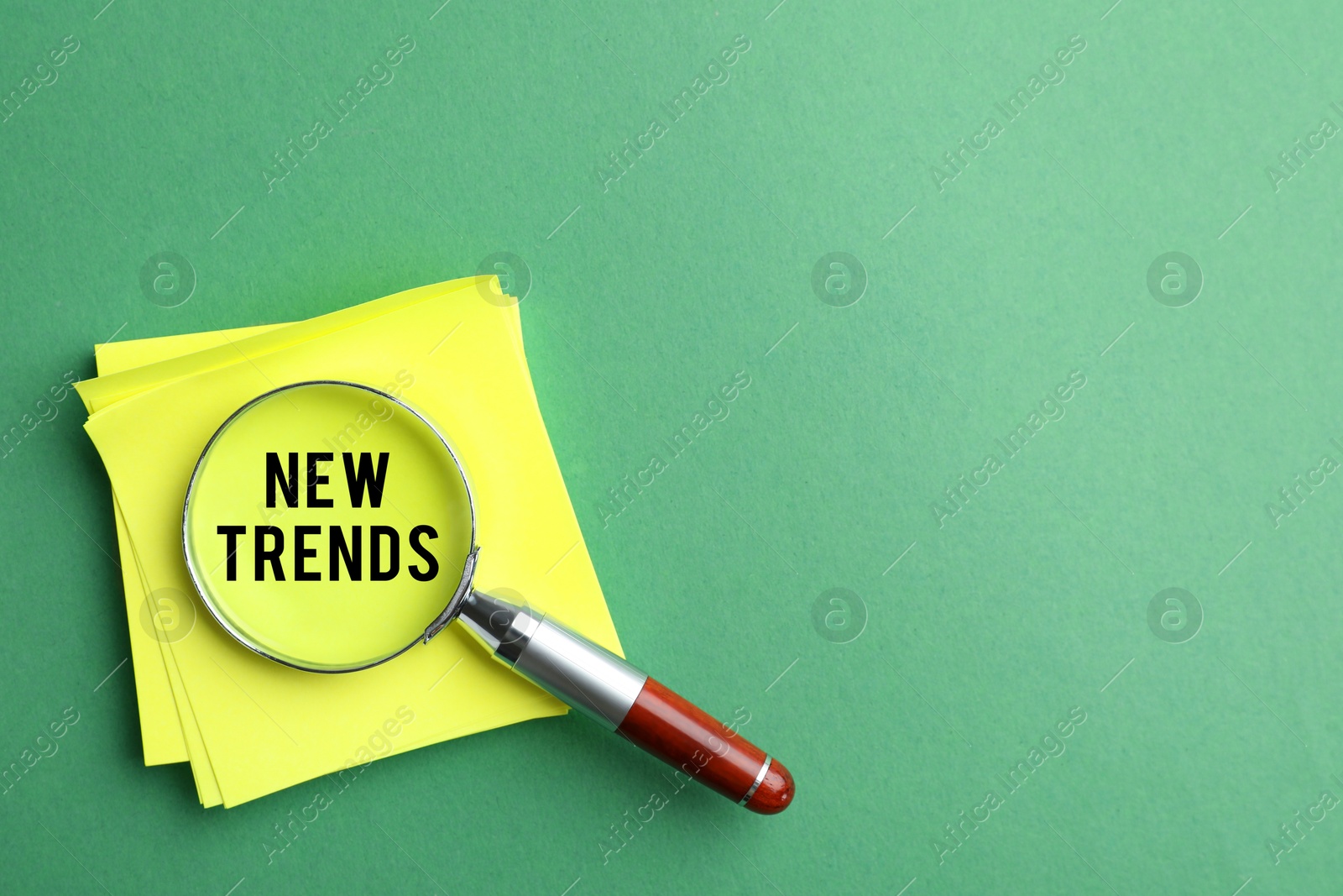 Image of Paper note with words New Trends on green background, view through magnifying glass. Concept of searching for fresh and popular ideas