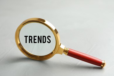 Image of Word Trends in magnifying glass on grey background, closeup. Concept of searching for new and popular ideas