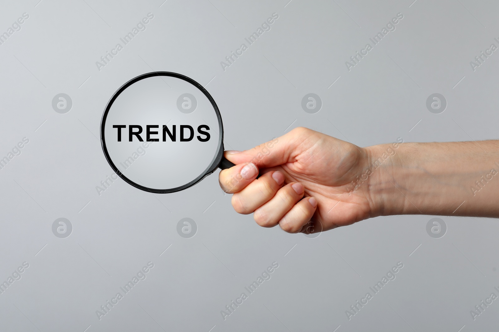 Image of Woman looking at word Trends through magnifying glass on grey background, closeup. Concept of searching for new and popular ideas