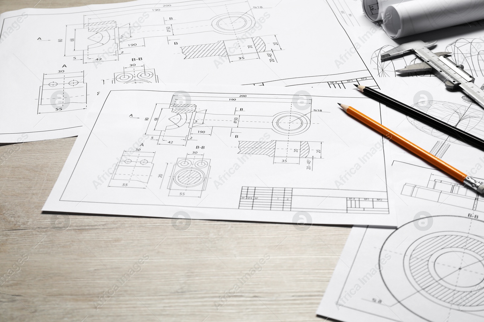 Photo of Different engineering drawings, vernier caliper and pencils on wooden table, closeup