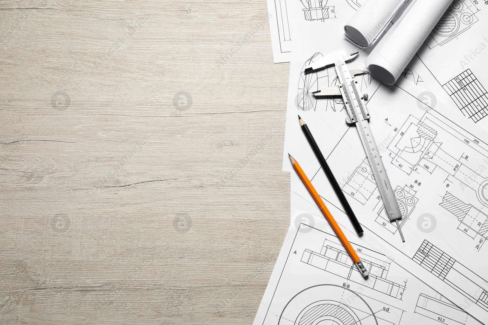 Photo of Different engineering drawings, vernier caliper and pencils on wooden table, top view. Space for text