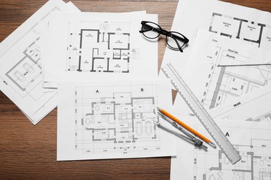 Photo of Different architectural drawings, pencil, ruler, glasses and divider on wooden table, flat lay