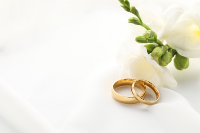 Golden wedding rings and flowers on white fabric, closeup. Space for text