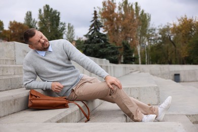 Photo of Man with injured leg on stairs outdoors after fall. Dangerous accident