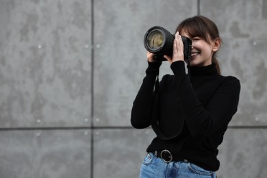 Photo of Professional photographer taking picture with camera near grey wall outdoors. Space for text