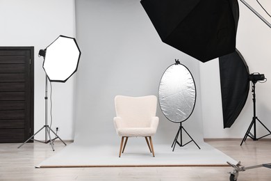 Photo of Professional lighting equipment setup and armchair in modern photo studio