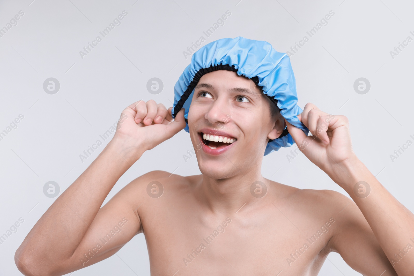 Photo of Happy man wearing shower cap on light grey background