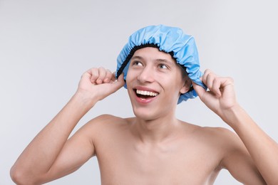 Photo of Happy man wearing shower cap on light grey background