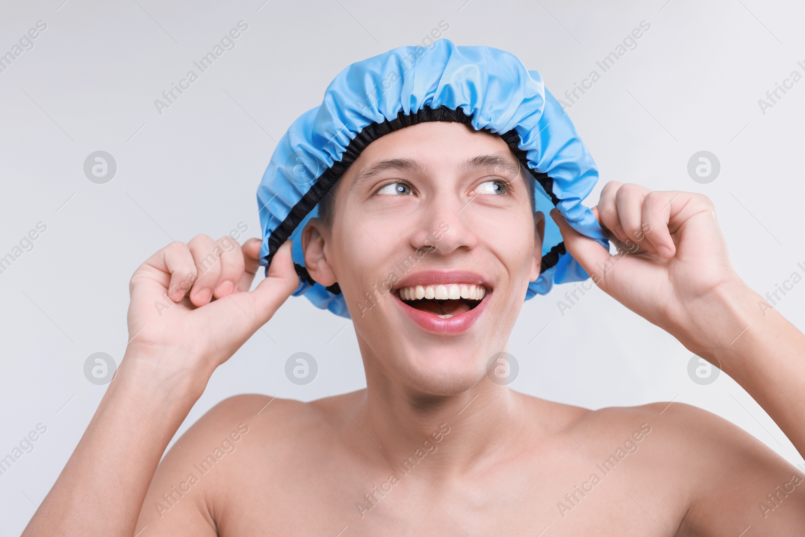 Photo of Happy man wearing shower cap on light grey background