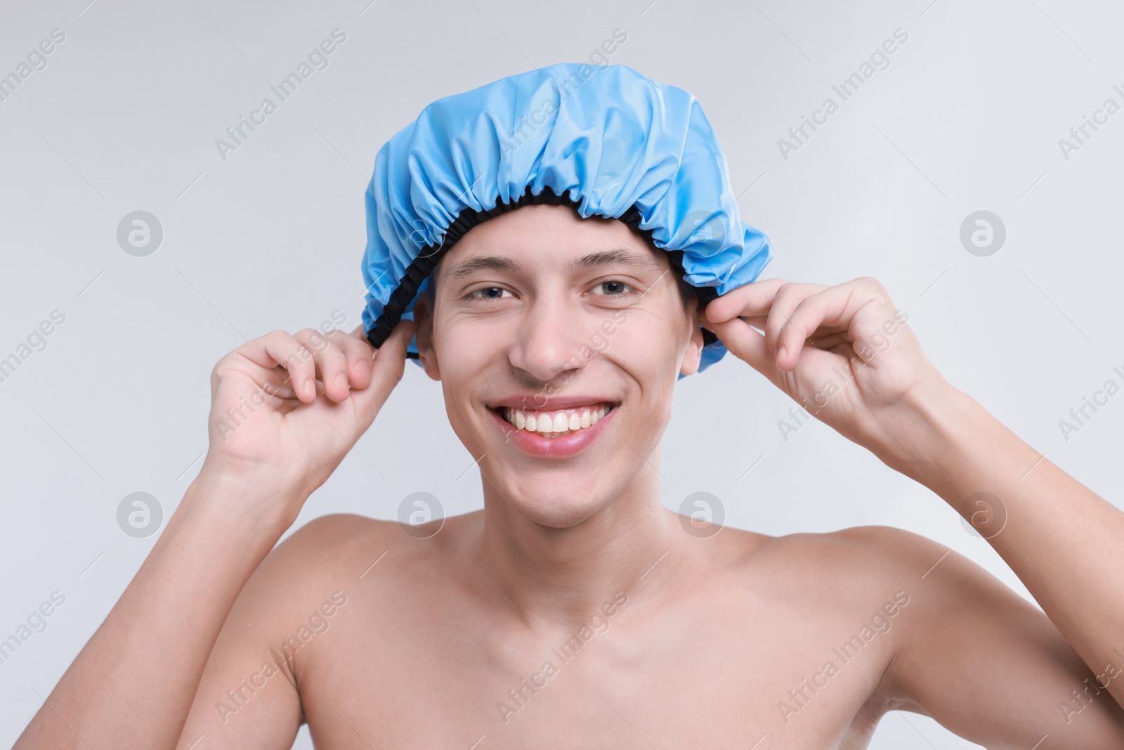 Photo of Happy man wearing shower cap on light grey background