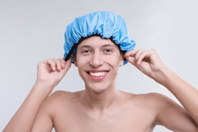 Photo of Happy man wearing shower cap on light grey background