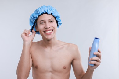 Photo of Man with shower cap and shampoo on light grey background