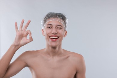 Photo of Man in shower cap showing ok gesture on light grey background