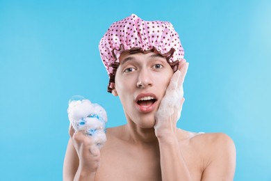 Photo of Man with shower cap and mesh sponge on light blue background