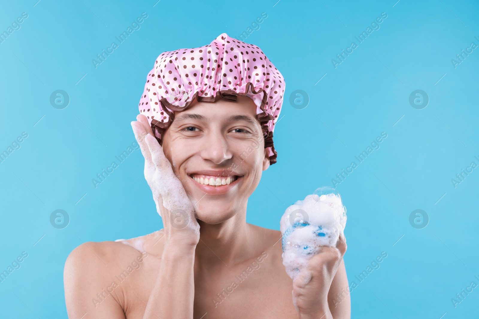 Photo of Man with shower cap and mesh sponge on light blue background